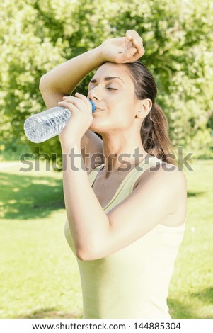Fitness girl refreshment drinking water in the park.