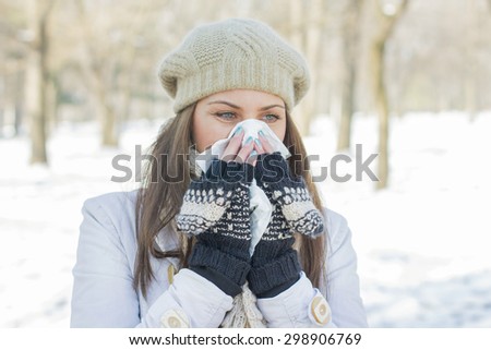 Young Woman in Winter Clothing  Blowing Nose with tissue paper outdoor. Caucasian female in snow park sneezing.