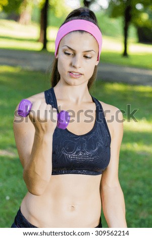 Fitness Slim Woman Training with dumbbells. Female practicing using hand weights outdoor. Healthy lifestyle workout concept on beautiful summer day.