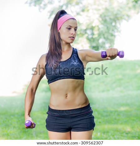 Fitness Slim Woman Training with dumbbells. Female practicing using hand weights outdoor. Healthy lifestyle workout concept on beautiful summer day.