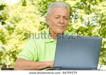 Elderly man using laptop in the park.