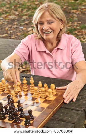 Smiling senior women playing chess on a park bench.