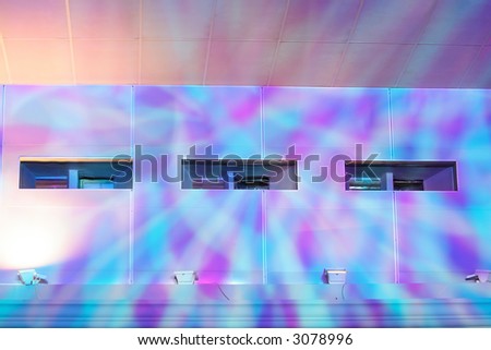 Holes of projection booth in a wall lit by purple and blue