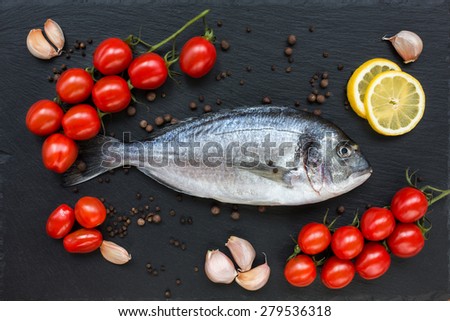 Fresh dorado fish on slate cutting board with lemon, garlic and cherry tomatoes