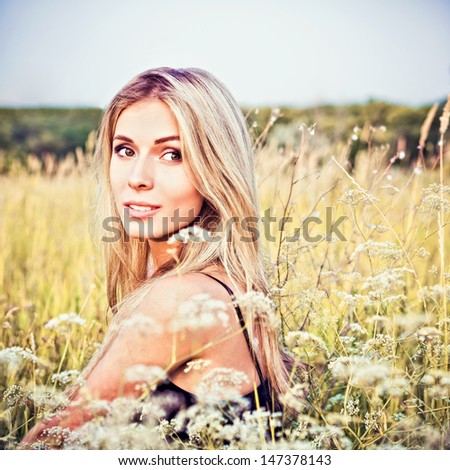 A beautiful smiling young girl sitting among the grass and flowers