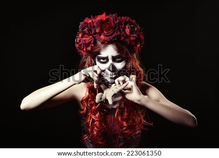 Young voodoo witch with muertos makeup (sugar skull) piercing a doll