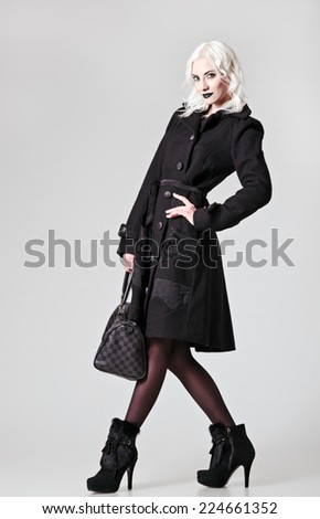Studio fashion shot: beautiful girl in black coat and boots, with bag in hand