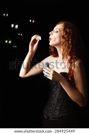 A beautiful redhead girl blows bubbles. Studio portrait, profile view