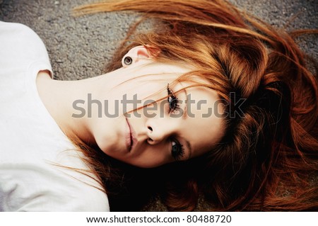 Closeup portrait of beautiful young girl lying on asphalt