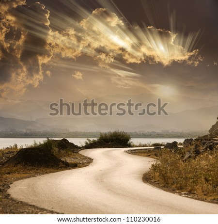snake road under dramatic sky with sun rays