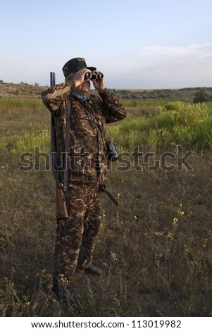 man with gun looking in binoculars for a duck