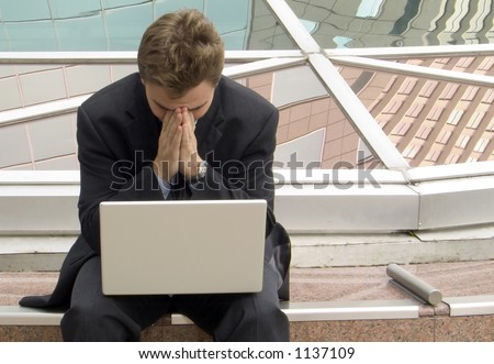 Business man with his head in his hands, a laptop on his lap.