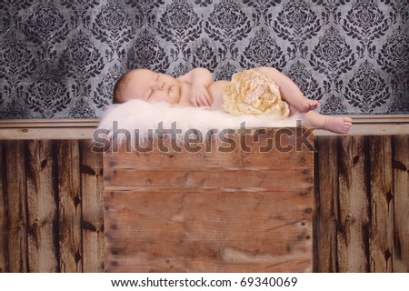 Tiny baby sleeping on a  vintage wooden box with vintage wallpaper behind.