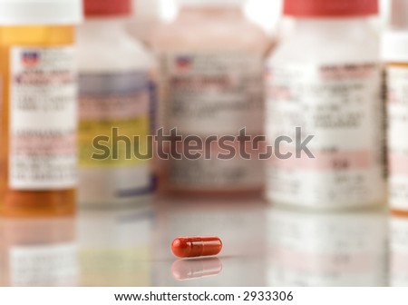 Close up of red pill and prescriptions on a high key background.  The focus is on a pill and falls off quickly.