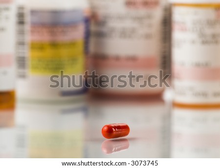 Close up of red pill and prescriptions on a high key background. The focus is on the pill and falls off quickly