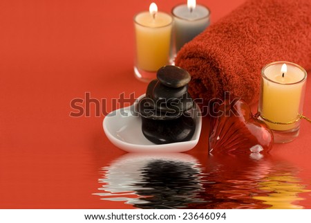 red towel, candles, river stones in heart shaped plate and red heart on red background with soft focus reflected in the water