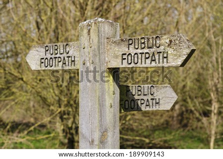 Public footpath sign pointing three ways against a forest background