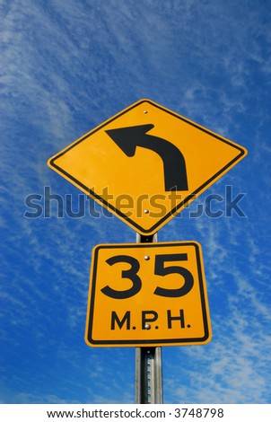 Yellow and black road sign with curved arrow, against blue sky