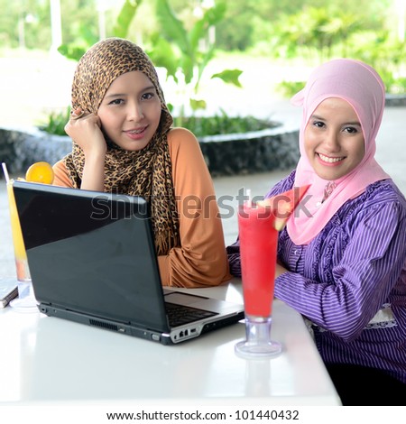 Two young pretty Asian muslim business woman in head scarf with book laptop
