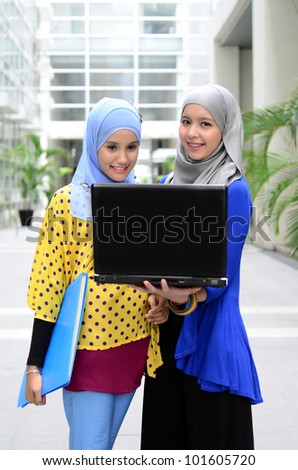 Two young pretty Asian muslim business woman in head scarf with book and laptop