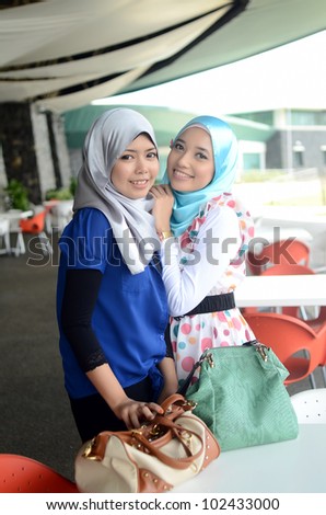 Two young pretty Asian muslim in head scarf smile in cafe