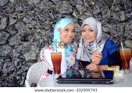 Two young pretty Asian muslim business woman in head scarf with laptop