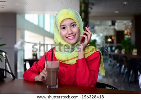 Young asian muslim woman in head scarf smile with mobile phone at cafe