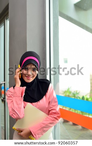 Portrait of young beautiful Asian Muslim women to talk business with a mobile phone while holding a file