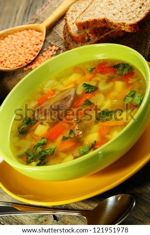 Chicken soup with red lentils in green cup on a wooden table.