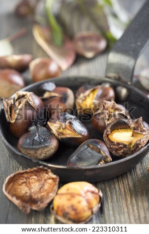 Frying pan with roasted chestnuts on an old table.