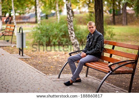 Handsome guy sitting outdoors on a bench and looking into the distance