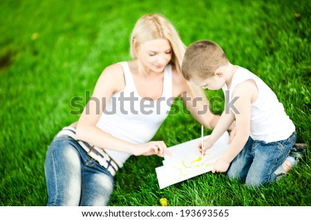 Son drawing with mother on the grass in the park in spring