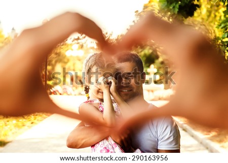 Handsome man hold a baby and looking at the camera through the heart of the fingers smiling and feeling happy