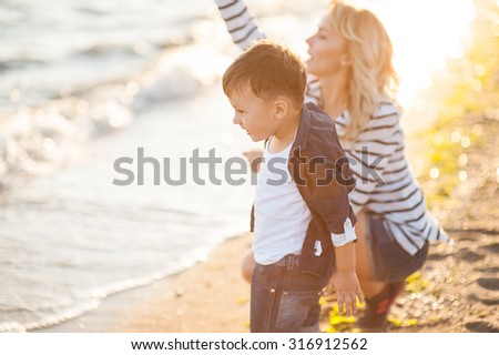 Beautiful boy with a woman relaxing on the beach. Throw pebbles into the sea, running, jumping, laughing and having a great time with each other at sunset.