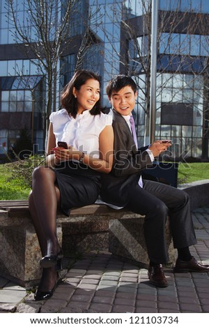 Business couple sitting on the bench chatting with mobile phone