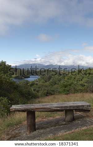 A lone bench on top of a hill overlooking a lake and a mountain