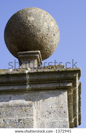 Round stone ball on top of pillar. Part of an old manor house gate post set against bright blue sky.