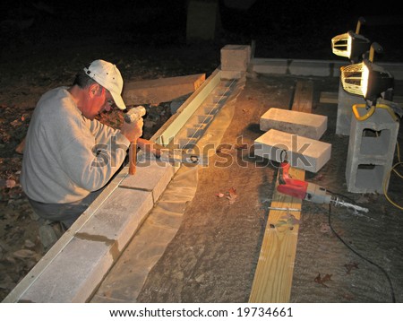 Mason laying block wall at night under lights