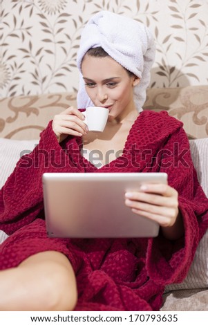 Beautiful girl in bathrobe drinking coffee  and watching news on tablet pc