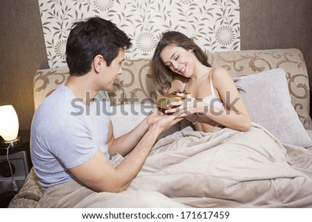 Man giving woman gift box in bed