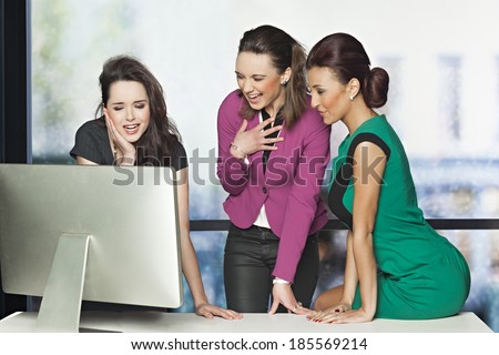 Business women in the office laughing while watching funny video - reaction concept