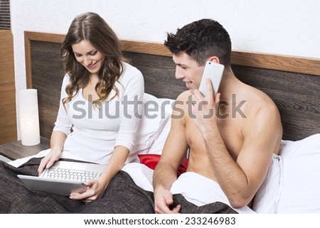 Attractive young woman working on the notebook, boyfriend talking on the phone