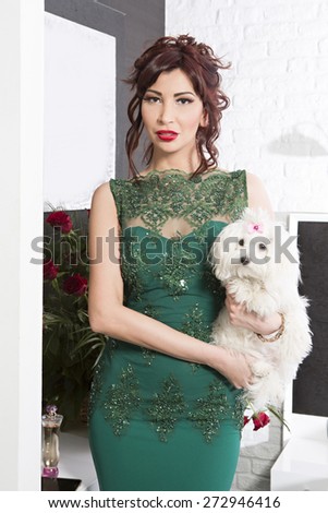 Attractive woman in elegant dress holding dog in hotel room
