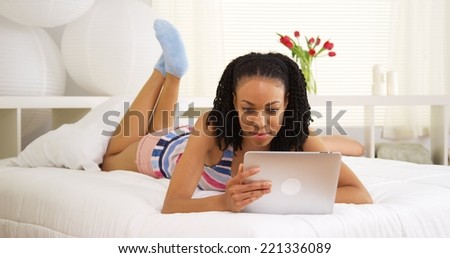 Happy African woman using tablet on bed