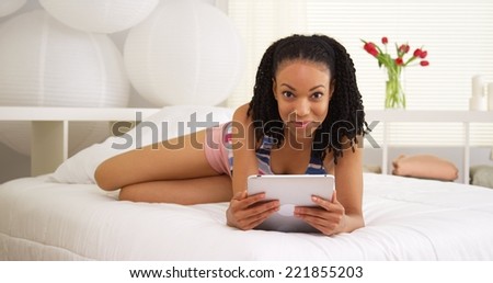 Black woman smiling at camera with tablet in bedroom
