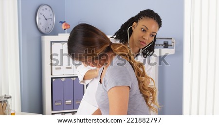 African American doctor listening to heart and lungs of Asian patient