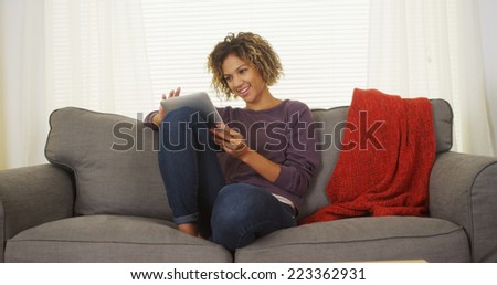 Happy black woman sitting on couch using tablet