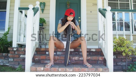 Hispanic woman sitting on porch with skateboard