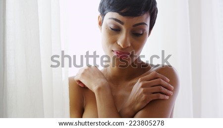 Beautiful topless black woman hugging herself and standing by window