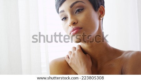 Beautiful topless black woman hugging herself and looking out window